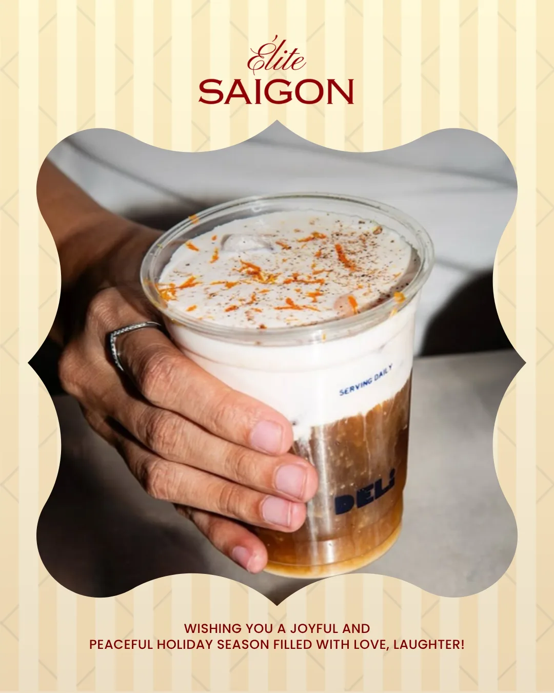 A hand holding a takeaway cup of iced coffee topped with thick foam, dusted with orange zest and cocoa
